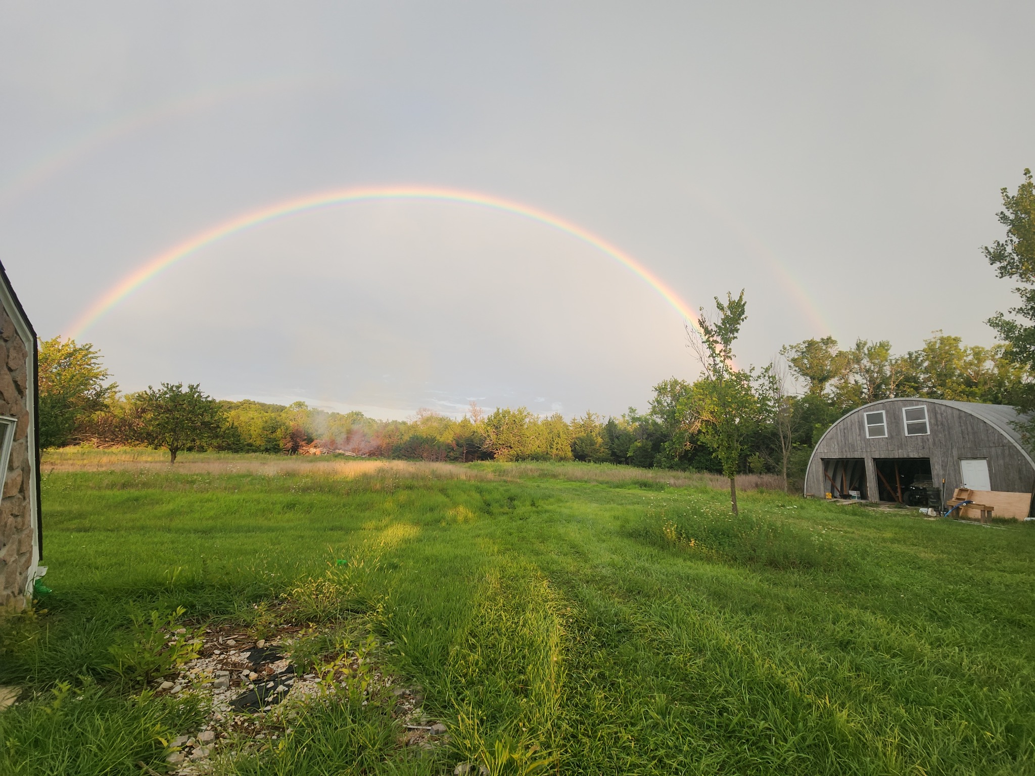 A rainbow stretches over green pasture, trees, and the ranch barn.